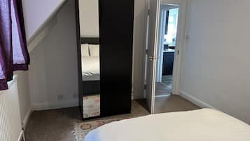 A bedroom with a bed, a large mirror, and a door leading to another room.