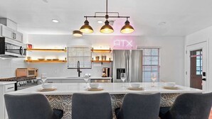 A modern kitchen with a central island, bar stools, and a neon sign. - Hollywood Vibe Cottage | Game Rm | Near Rainy St. (Austin)