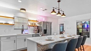 A modern kitchen with a central island, stainless steel appliances, and a neon sign. - Hollywood Vibe Cottage | Game Rm | Near Rainy St. (Austin)