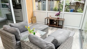 Un espace extérieur moderne, aménagé avec des meubles en osier et doté d’une porte en verre donnant sur un jardin.