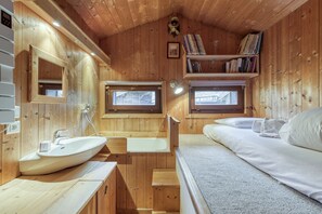 L’intérieur d’un chalet en bois comprend un lavabo en forme de bateau, une baignoire, un lit et une bibliothèque remplie de livres.