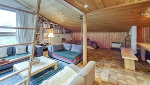 A cozy cabin interior with a loft bed, a sofa, a dining table, and a bookshelf filled with books. - Apt Le Grenier Ski-in/Ski-out views, sleeps 7, Le Tour (Argentière), France (Le Tour (Argentière))