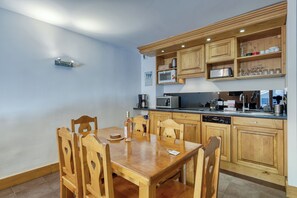 A modern kitchen with wooden cabinets, a dining table, and various appliances. - V Loriaz 32: Beside Ski Lift; Pool, Sauna & Gym, Vallorcine (Argentiere), France (Vallorcine (Argentiere))