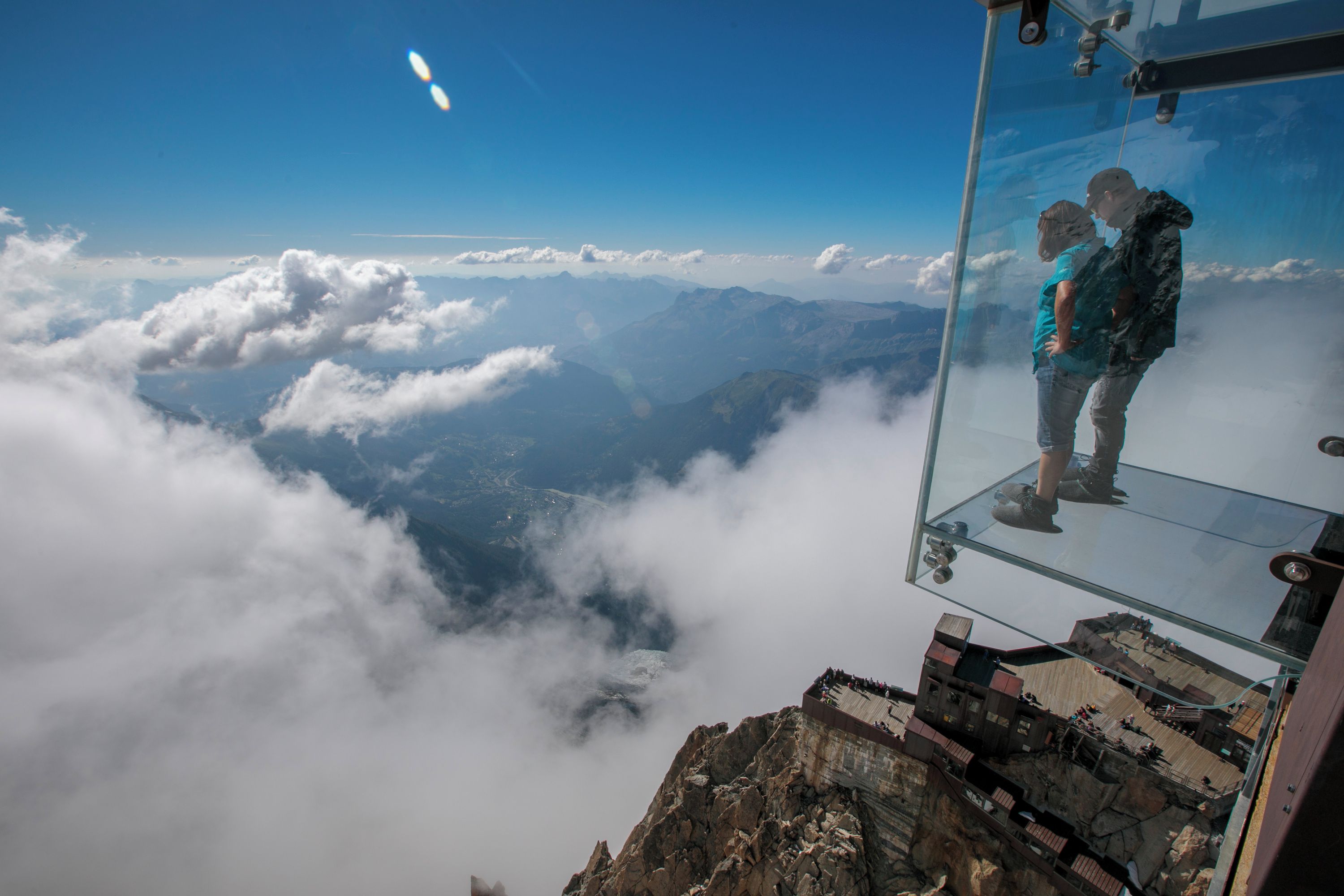 Une plateforme d’observation en verre offrant une vue dégagée sur les nuages et les montagnes.