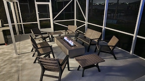 Un espace extérieur abrité, aménagé avec un foyer, des chaises et des tables.