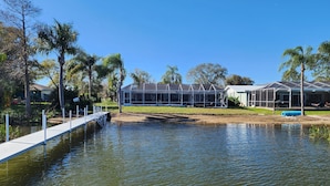 Un hôtel situé au bord d’un lac, avec une jetée qui s’avance sur l’eau, entouré de palmiers et surplombé d’un ciel bleu azur.