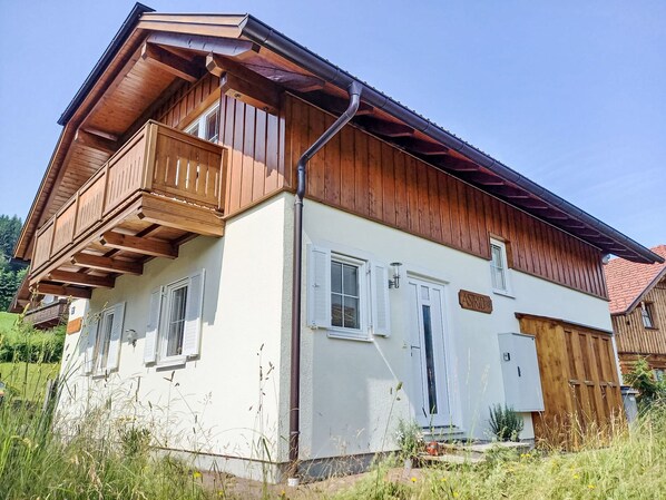 Une maison en bois à deux étages, dotée d’un balcon, de murs extérieurs blancs et d’une porte en bois.