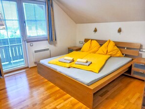 Une chambre à coucher avec un lit en bois, une literie jaune, une table de chevet et une fenêtre avec des stores.