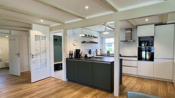 A modern kitchen with a central island, wooden flooring, and white cabinetry. - Melvill by Interhome (Dittishausen)