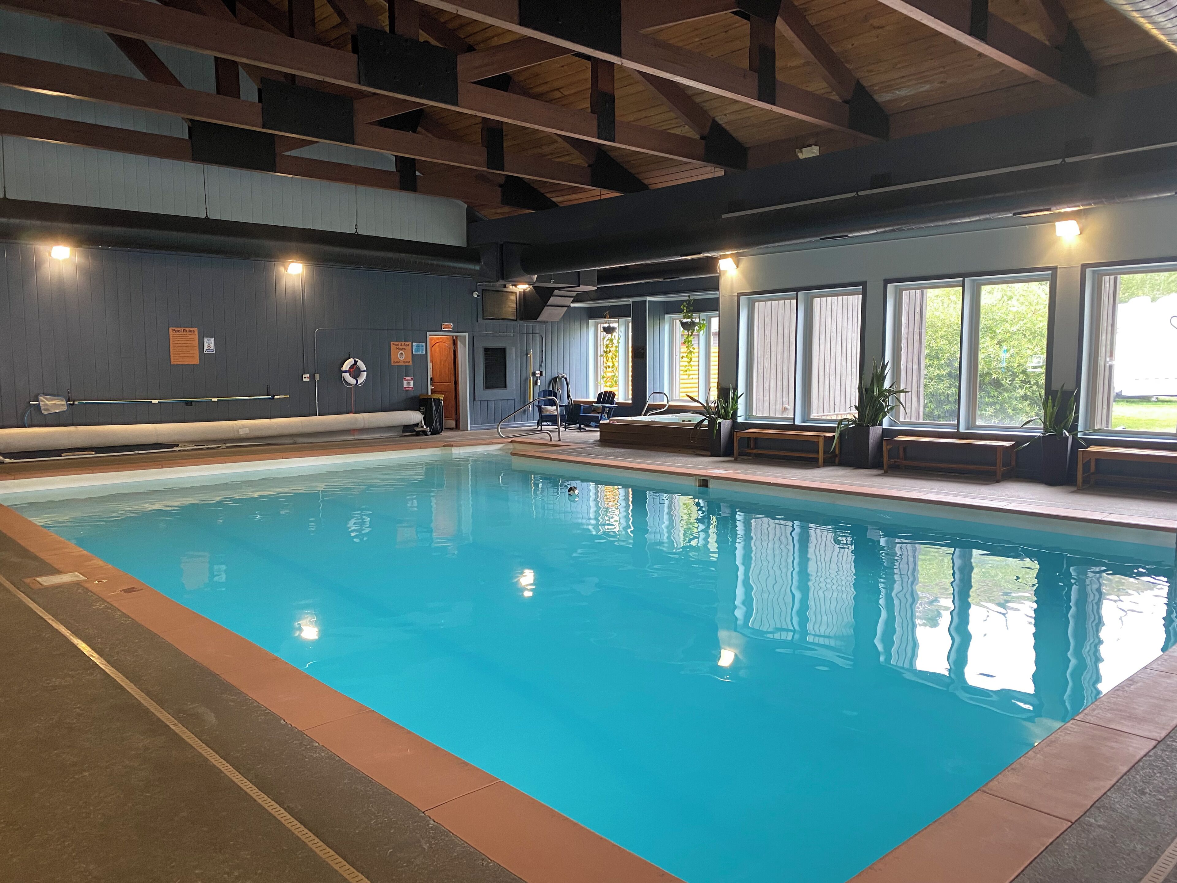 Una piscina interna con acqua cristallina, panche di legno e finestre che offrono vista sul verde circostante.