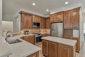 A modern kitchen with wooden cabinets, stainless steel appliances, and a marble countertop. - The Woodlands 4BR Executive Retreat - EV, Baby & Pet Friendly, Near Hospitals (Spring)