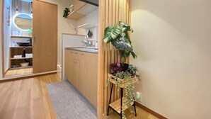 A modern kitchen with wooden cabinets, a built-in sink, and a countertop. There is a wooden plant stand with various plants. - G1A#[NEW] Tokyo/Shinjuku-ku/New comfortable guest room/5 min. to Shinjuku on JR line (新宿区)