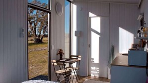 A room with a large sliding glass door leading to an outdoor area, a small table with chairs, and a kitchenette area. - Orana Cabin by Tiny Away (Cherry Tree Pool)