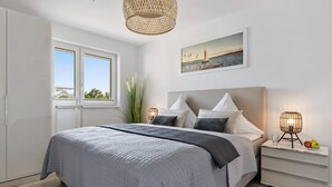 Un dormitorio con una cama grande, una ventana con vistas, una mesita de noche con lámpara y un cuadro en la pared.
