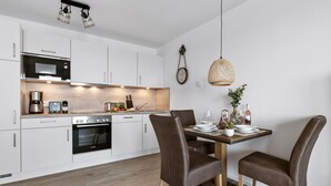 Una cocina moderna con armarios blancos, un horno Bosch y una zona de comedor con mesa de madera y sillas marrones.