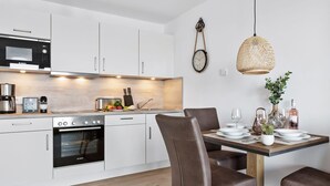 Una cocina moderna con armarios blancos, un microondas Bosch y una cafetera. Hay una mesa de comedor con sillas y una lámpara colgante.