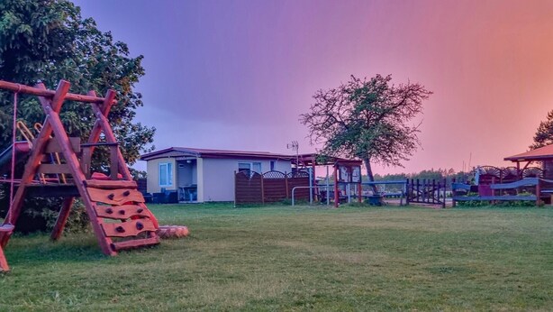 A playground with swings and a slide, a fenced area, and a building with a red roof.