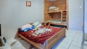 A bedroom with a wooden bunk bed, a red floral bedspread, and a small bedside table.
