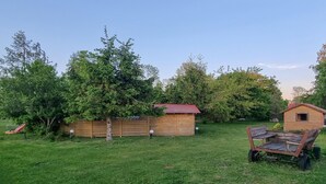 A grassy backyard with a wooden shed, a small wooden structure, and a wooden cart.