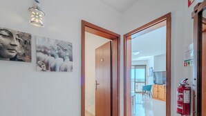Un pasillo con una puerta de madera que da a un balcón, un extintor y una lámpara fijada a la pared.