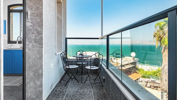 Un balcón con mesa y sillas, vista al mar y una puerta azul.