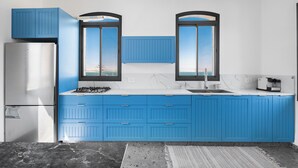 Una cocina moderna con armarios azules, un refrigerador blanco y un ventanal con vista al mar.