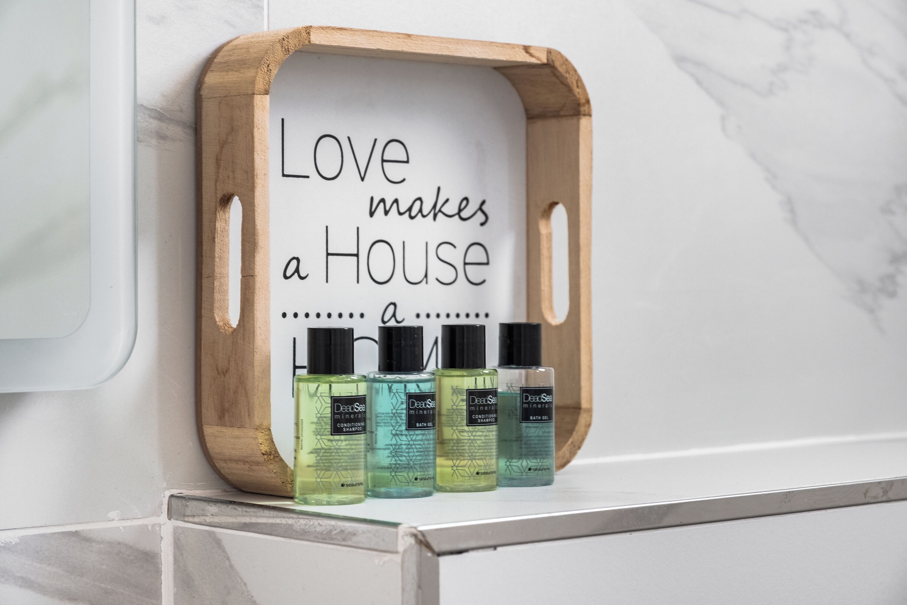 A wooden tray with a sign saying "Love makes a House" and three bottles of DearSea shampoo.