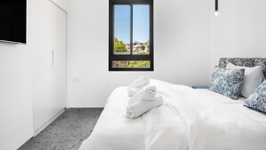 Un dormitorio con cama, ventana con vistas, televisor y lámpara colgante.
