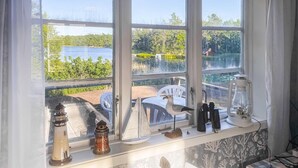 Ein Zimmer mit Fensterblick auf einen See, ein weißer Stuhl und verschiedene Dekorationen auf der Fensterbank.