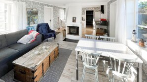 Ein gemütliches Wohnzimmer mit einer Couch, einer Holzbank und einem Esstisch mit Stühlen. Im Hintergrund ist ein Kamin zu sehen.