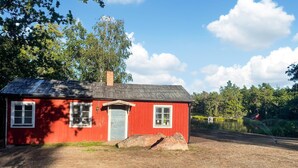 Ein rotes Holzhaus mit grauer Tür, zwei Fenstern und einem Schornstein.