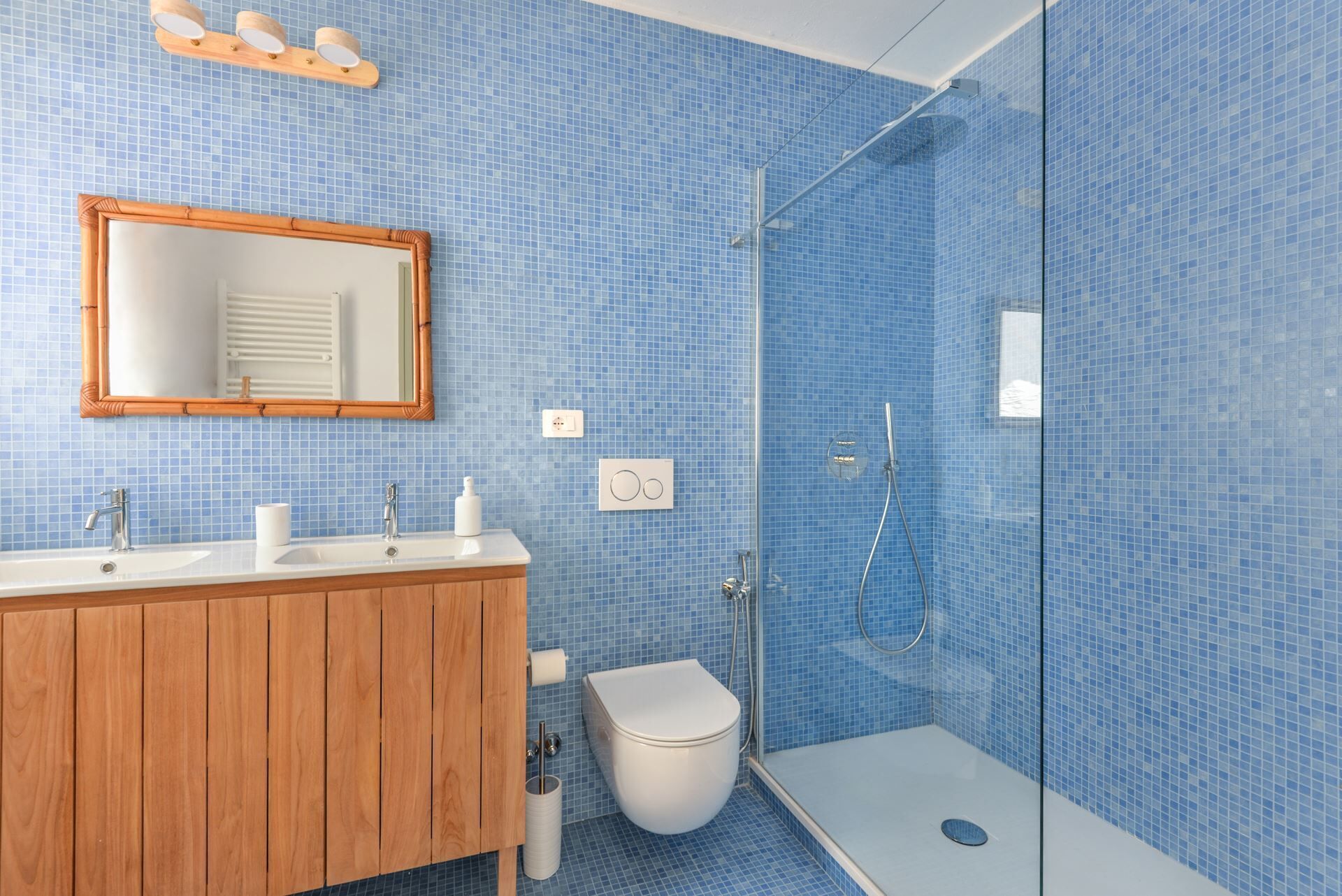 A bathroom with a wooden vanity, a mirror, a toilet, and a glass-enclosed shower area.