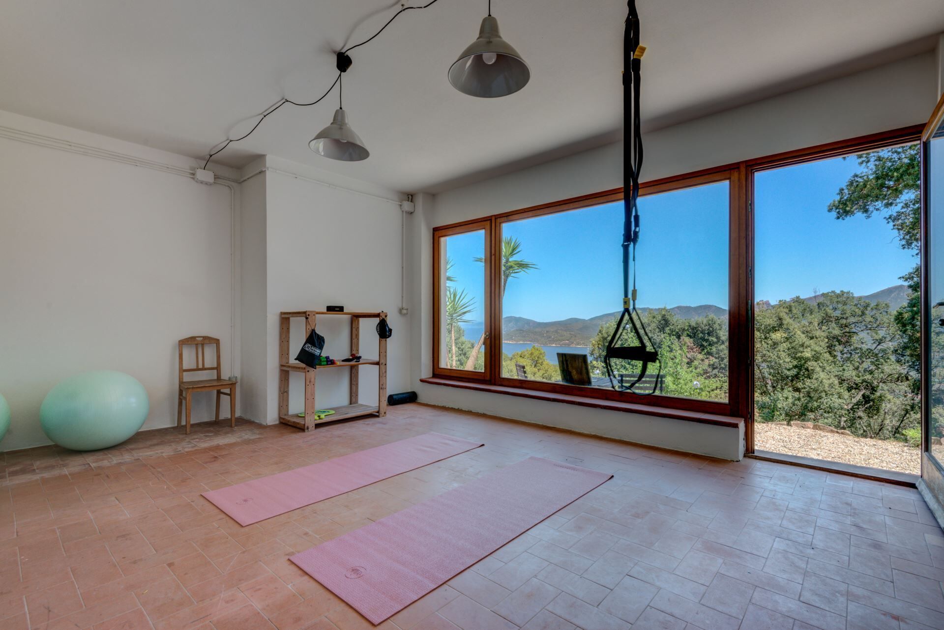 A spacious room with a large window, wooden flooring, and exercise equipment.