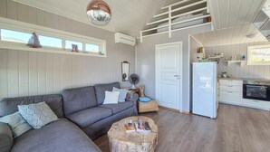 Un salon moderne avec un canapé gris, une table basse en bois et un coin cuisine comprenant un réfrigérateur et une cuisinière blancs.
