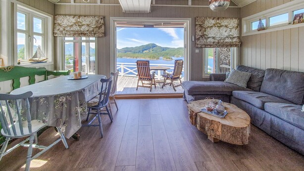 Une pièce chaleureuse comprenant une table à manger, des chaises, un canapé et une table basse. Les fenêtres offrent une vue sur un lac et des montagnes.