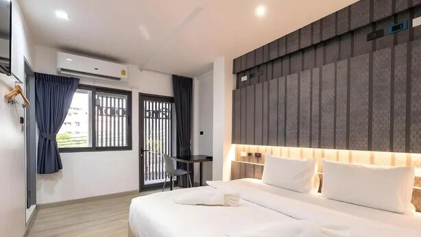 A modern hotel room with a large bed, a desk, and a view through a window with a balcony. - Baan Kun Mhor Hostel (Bangkok)