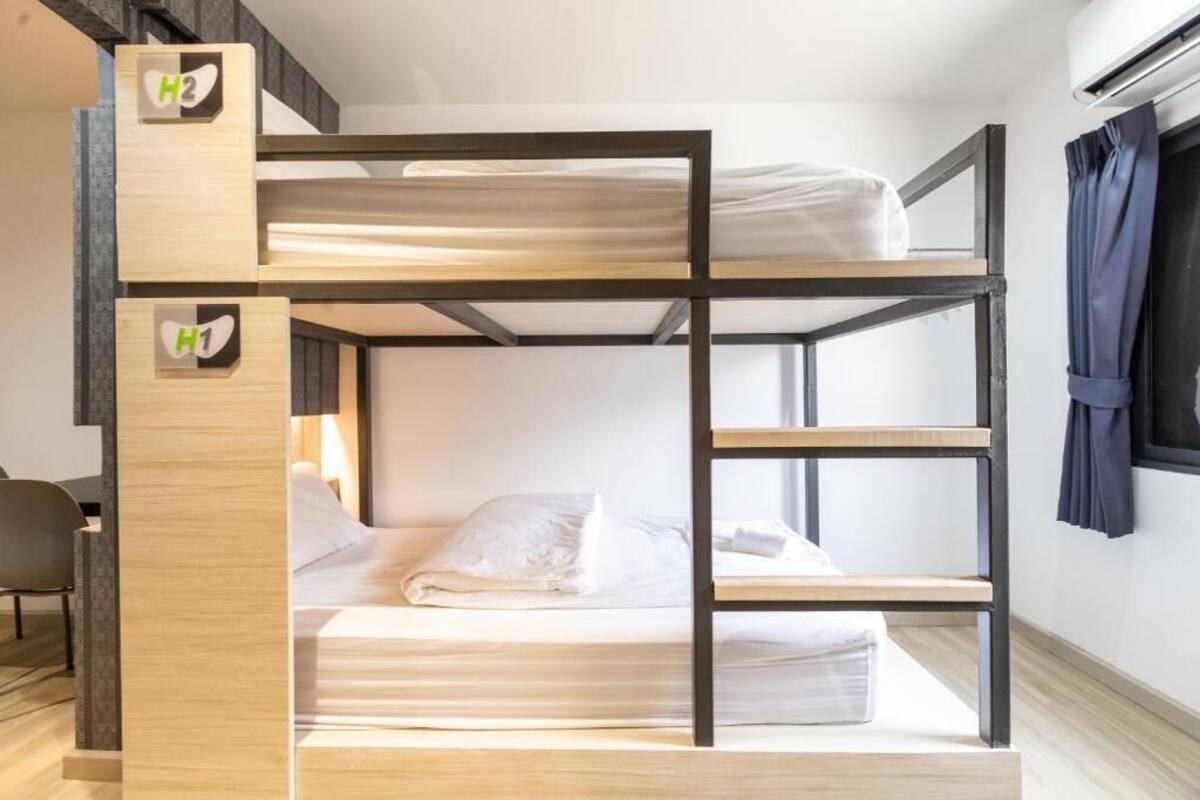 Un lit superposé à deux niveaux, chaque niveau étant équipé d’un matelas et d’oreillers. Il y a aussi une chaise et une fenêtre avec des rideaux.