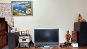 Un salon doté d’un téléviseur à écran plat, d’un meuble de rangement en bois et d’un tableau représentant un paysage côtier.