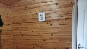Una habitación con paneles de madera, una cama, una mesita de noche, una lámpara roja y una puerta.