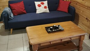 Una habitación con paneles de madera, un sofá azul, cojines rojos, una mesa de centro de madera y un espejo en la pared.