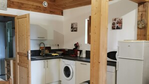 Cocina compacta con vigas de madera, lavadora, refrigerador y cubo de basura.