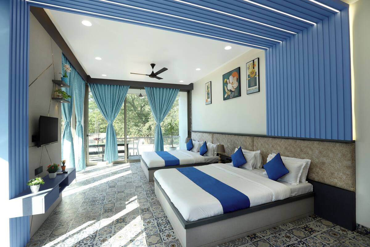 A modern hotel room with two beds, a ceiling fan, a TV, and a balcony with curtains.