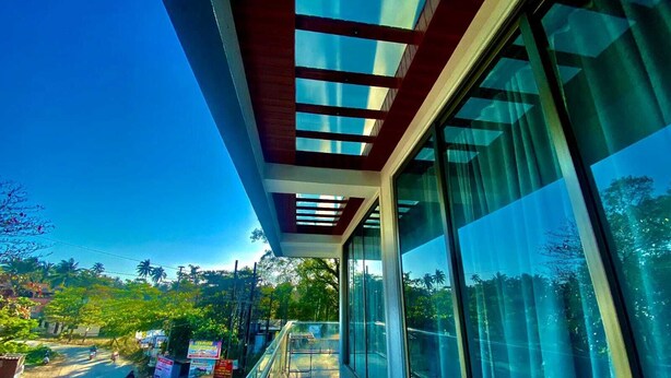 A modern building with large windows and a balcony overlooking a street with parked motorcycles and greenery. - Sandhya Manohar Beach Resort (Alibag)