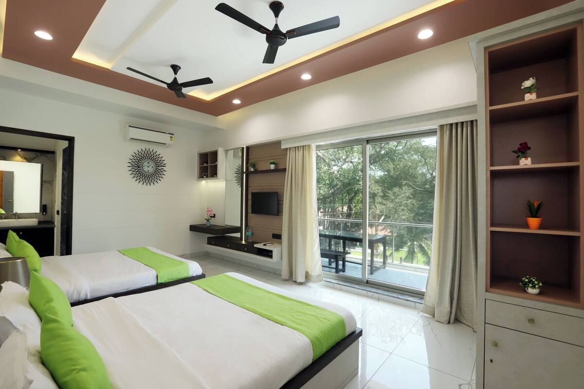 A modern hotel room with two beds, a ceiling fan, a large window with a view, and built-in shelves.