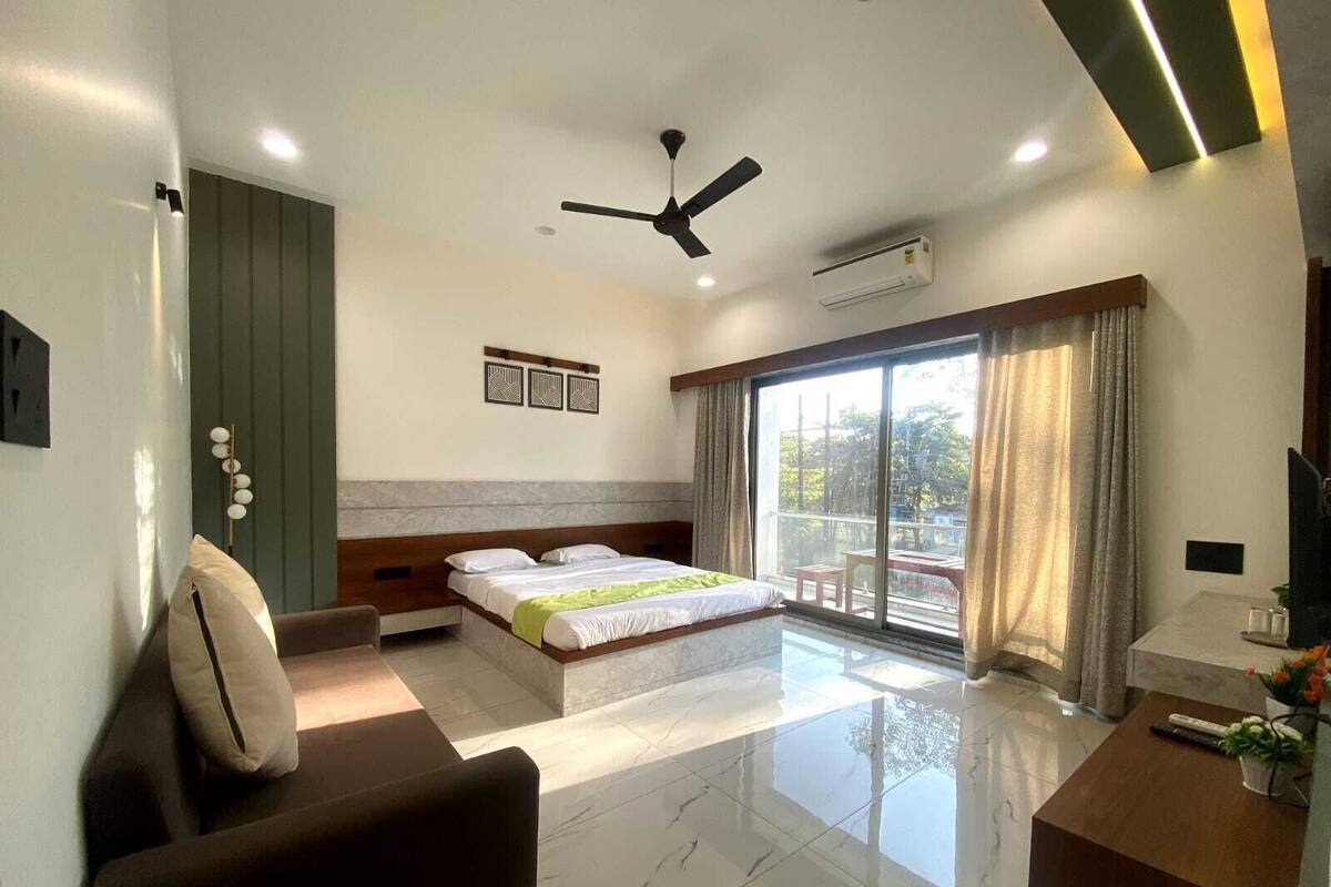 A modern hotel room with a bed, a desk, a chair, a ceiling fan, and a large window with curtains.