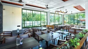 A restaurant with multiple tables and chairs, large windows, and ceiling fans. - Sandhya Manohar Beach Resort (Alibag)