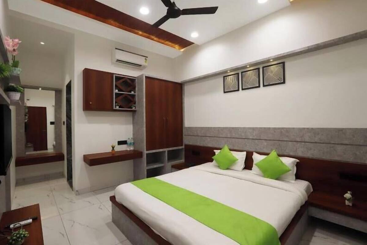 A modern hotel room with a large bed, a ceiling fan, built-in shelves, and a small seating area.