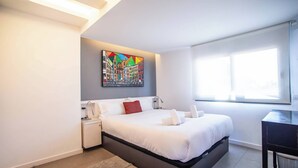 Une chambre moderne avec un grand lit, un bureau et un tableau coloré au mur.