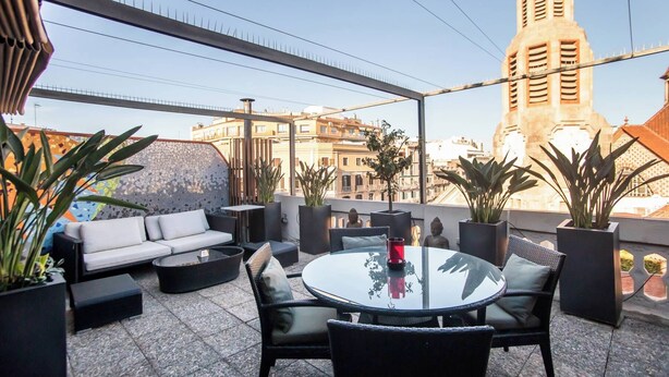 Une terrasse extérieure avec une table ronde, des chaises noires, un canapé et des plantes en pot.