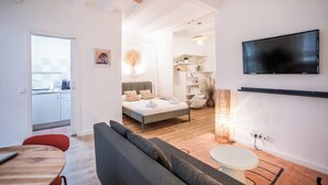 A modern living room with a sofa, a dining table, a TV mounted on the wall, and a ceiling fan.
